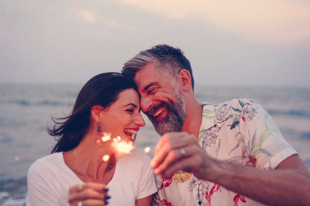 A middle age couple snuggles on the beach at sunset and holds up celebratory sparklers