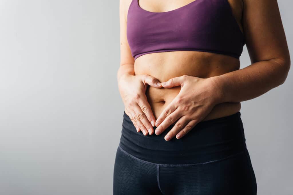 Woman holding hands in heart shape around her belly button