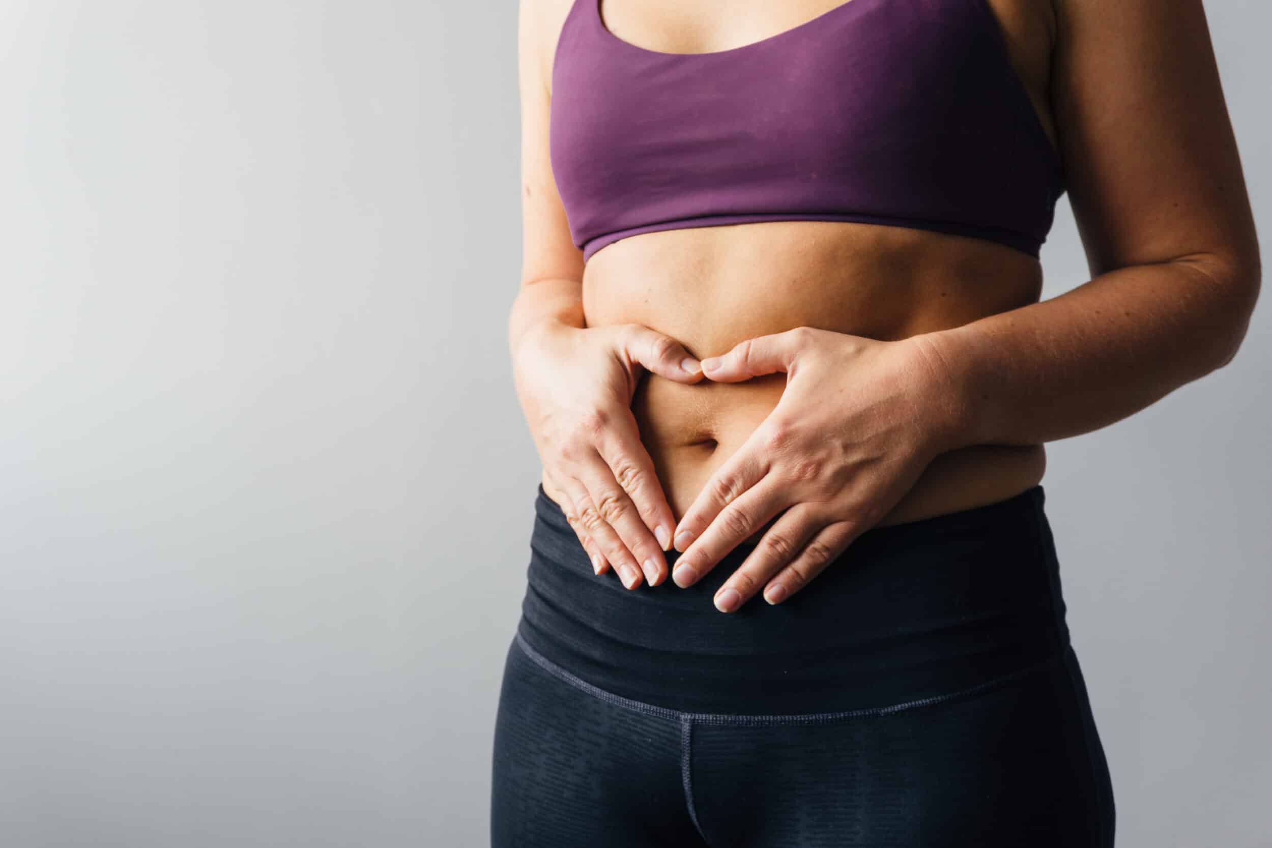 Woman holding hands in heart shape around her belly button