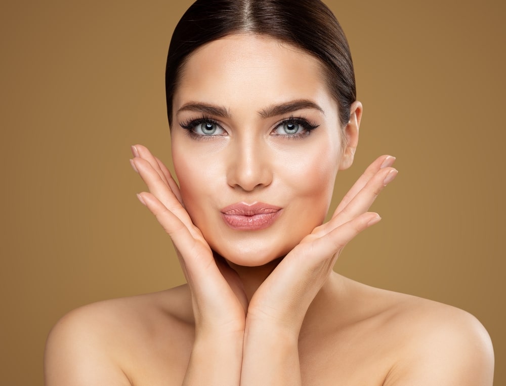 Woman with defined cheek contours and smooth skin holding her face, representing buccal fat removal for facial slimming.