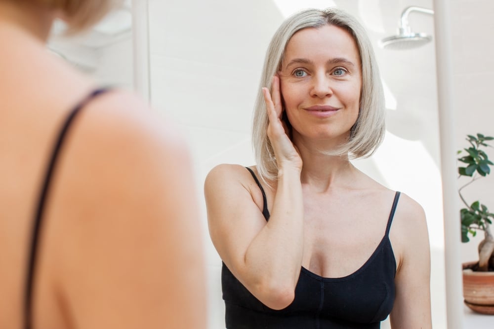Mature woman examining her skin and signs of aging in the mirror