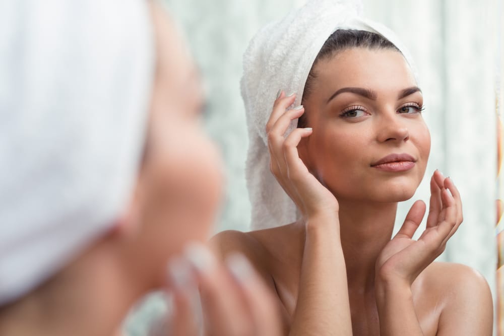Woman looking at her skin in the mirror after a shower